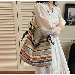 Dettaglio di una grande borsa tote in paglia a righe colorate con nodi decorativi sulle tracolle