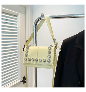 Detailed close-up of light yellow flap bag with silver rivets on wide shoulder strap