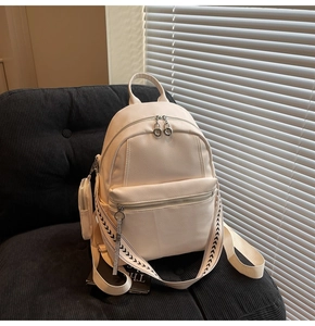 Detail of off-white leather backpack with decorative strap and mini coin pouch on a chair