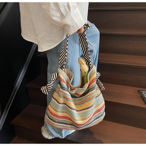 Dettaglio di una borsa tote in paglia a righe colorate con tracolla a motivi bianchi e neri