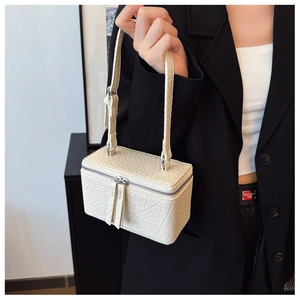 Detail of cream box bag showing faux crocodile embossed texture and dual tassel zippers