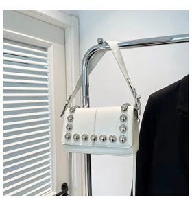 Detail of a white patent leather handbag featuring large silver spherical studs on edges