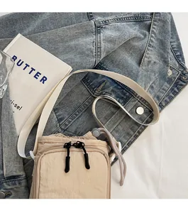 Detail of a beige nylon crossbody bag with drawstring closure on denim jacket background