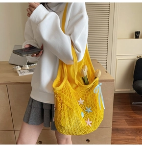 Yellow woven mesh tote bag with blue ribbon and charms shown in a lifestyle setting