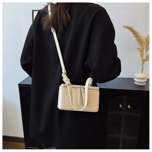 Detail view of cream textured crossbody box bag with metal zipper and leather shoulder strap