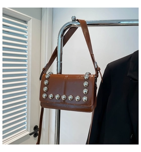 Detail of caramel brown patent leather crossbody bag with bold silver rivet studs