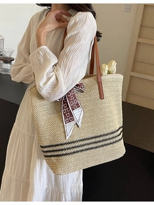 Minimalist straw tote bag with black stripes, leather handles, and decorative silk scarf