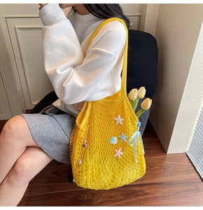 Detail of yellow knit tote bag featuring sea charms, beads, and floral ribbon accents