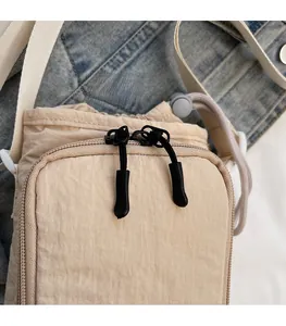 Detail of a smooth zipper on a beige nylon crossbody bag with drawstring design