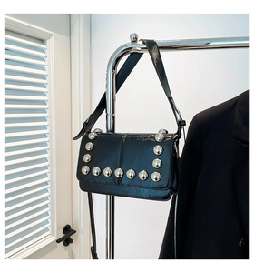Detail of a black punk style crossbody bag featuring rows of large silver round rivets