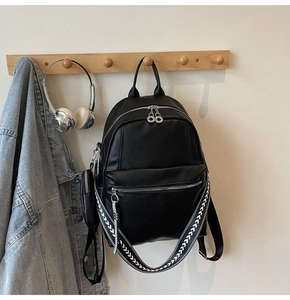 Close-up of black litchi texture leather backpack with wide geometric strap and mini charm