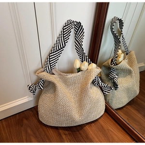 Dettaglio borsa tote in paglia beige con ampia tracolla in tessuto a righe bianche e nere