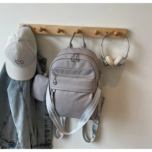 Close-up of light gray faux leather backpack with fabric strap and mini pouch charm