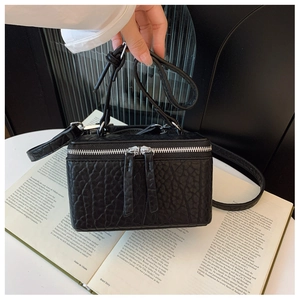 Detailed view of the black textured leather box bag with silver zippers and hand strap