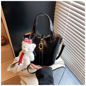 Vue détaillée du sac seau noir brillant avec anneaux métalliques et breloque ours blanc
