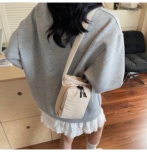 Close-up of beige nylon drawstring mini bag with adjustable strap and dual front zippers