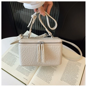 Detail of a creamy white box-shaped crossbody bag with textured leather and dual zippers