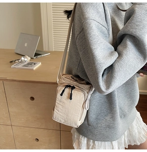 Detail of beige nylon crossbody bag featuring drawstring closure and zippered front pocket