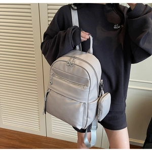 Detailed view of light gray faux leather backpack with multiple zip pockets on model