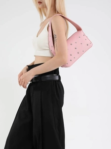 Borsa a spalla rosa con rivetti metallici argentati e tracolla larga indossata da modella