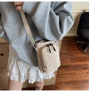 Detail of light beige drawstring crossbody bag in nylon with front zipper pocket and strap