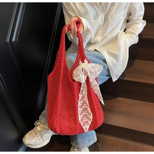 Détail du sac cabas en crochet rouge avec nœud en dentelle blanche sur bois sombre