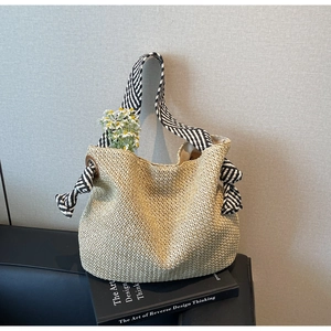 Dettaglio della borsa in paglia beige con tracolla in tela a righe e anello metallico