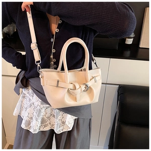 Détail du sac seau en cuir crème avec boucle argentée et bandoulière porté par un mannequin