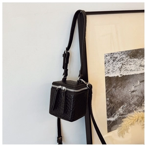Detail of a mini black cube crossbody bag with crocodile embossing and top zip closure
