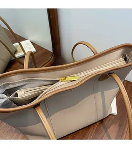 Detail of smooth gold zipper and hardware on a cream leather tote with brown handles