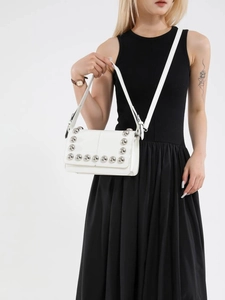 White minimalist crossbody bag with silver rivet studs on a model in a black outfit
