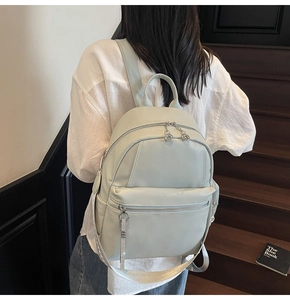 Detail of light grey lychee pattern leather backpack showing multiple zipper pockets