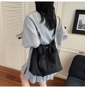 Detail view of black drawstring tote bag with functional side pockets on a model