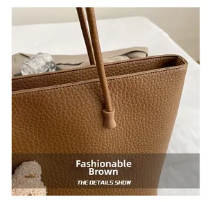 Close-up of litchi grain tote bag stitching with a cute bear charm and leather handle detail
