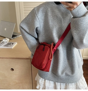 Detail of red nylon mini crossbody bag showing drawstring closure and front zip pocket