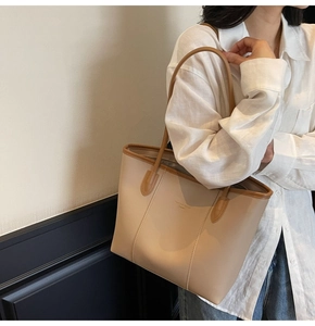 Close-up of a large beige and brown leather tote bag worn by a model for a chic daily look