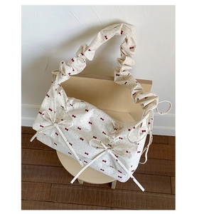 Détail d'un sac crème avec motifs de nœuds rouges et texture de bandoulière plissée