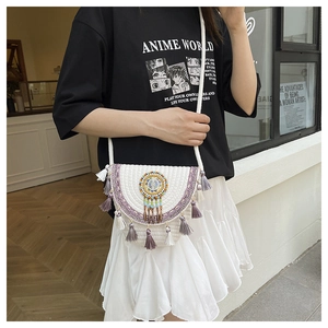 Dettaglio borsa di paglia boho con nappe viola, perline colorate e piume decorative