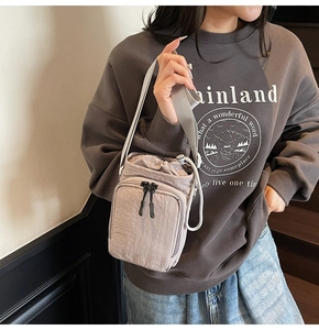 Detail shot of light gray nylon crossbody bucket bag worn by model on a stairway