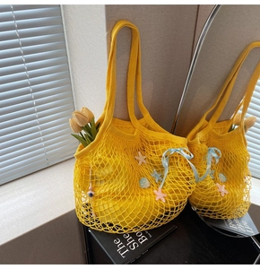 Detail of yellow woven tote bag featuring starfish shell charms and a blue silk bow