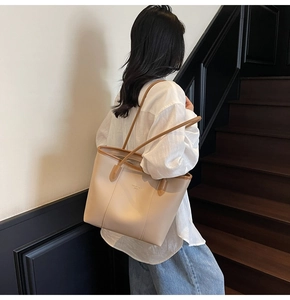Detail of cream tote bag with brown straps worn on shoulder by model on stairs