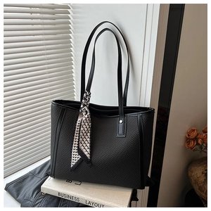 Detail of a large black tote bag with woven texture and checkerboard silk scarf handle