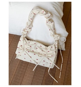 Détail du sac en tissu crème avec motifs de nœuds rouges et finitions de poignée à volants