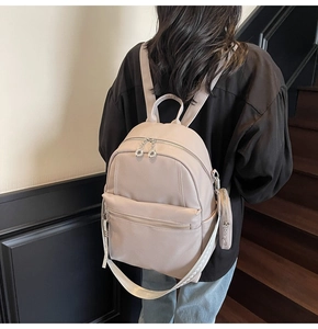 Detailed back view of a beige leather backpack with woven straps and a round coin purse