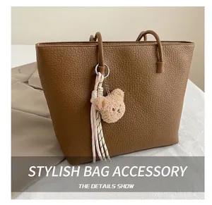 Detailed view of a plush bear charm with woven cord on a brown lychee leather tote bag