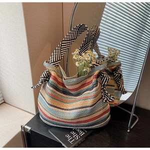 Dettaglio borsa tote in paglia a righe colorate con manici a fiocco e decoro margherita