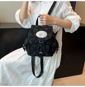 Detail eines schwarzen Mini-Rucksacks mit Blumenstickerei und silberner Markenplakette