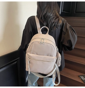 Close-up of beige pebbled leather backpack with metal ring zipper and side charm pouch