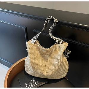 Dettaglio di una borsa tote in paglia intrecciata con tracolla a righe bianche e nere