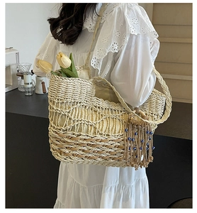 Detail of a beige woven straw tote bag with tassels and beads worn by a model in a cafe